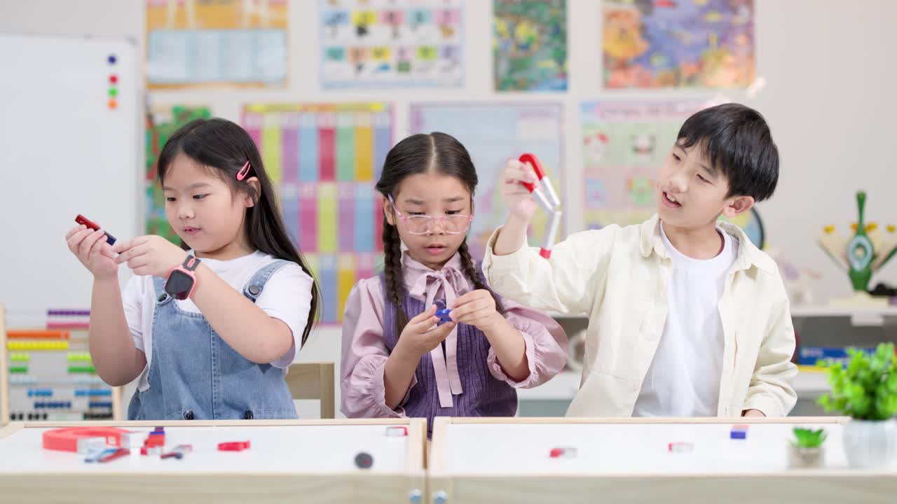 밝은 교실에서 세 명의 초등학생이 색색의 자석으로 실험을 하고 있습니다. 고정된 카메라 앵글, 즐거운 분위기.