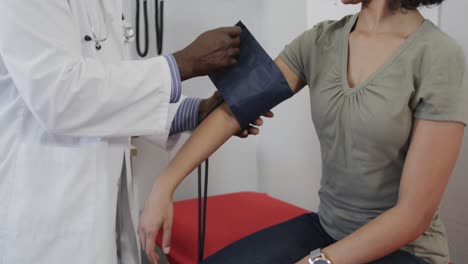 diverse male doctor examining female patient, measuring blood pressure, slow motion