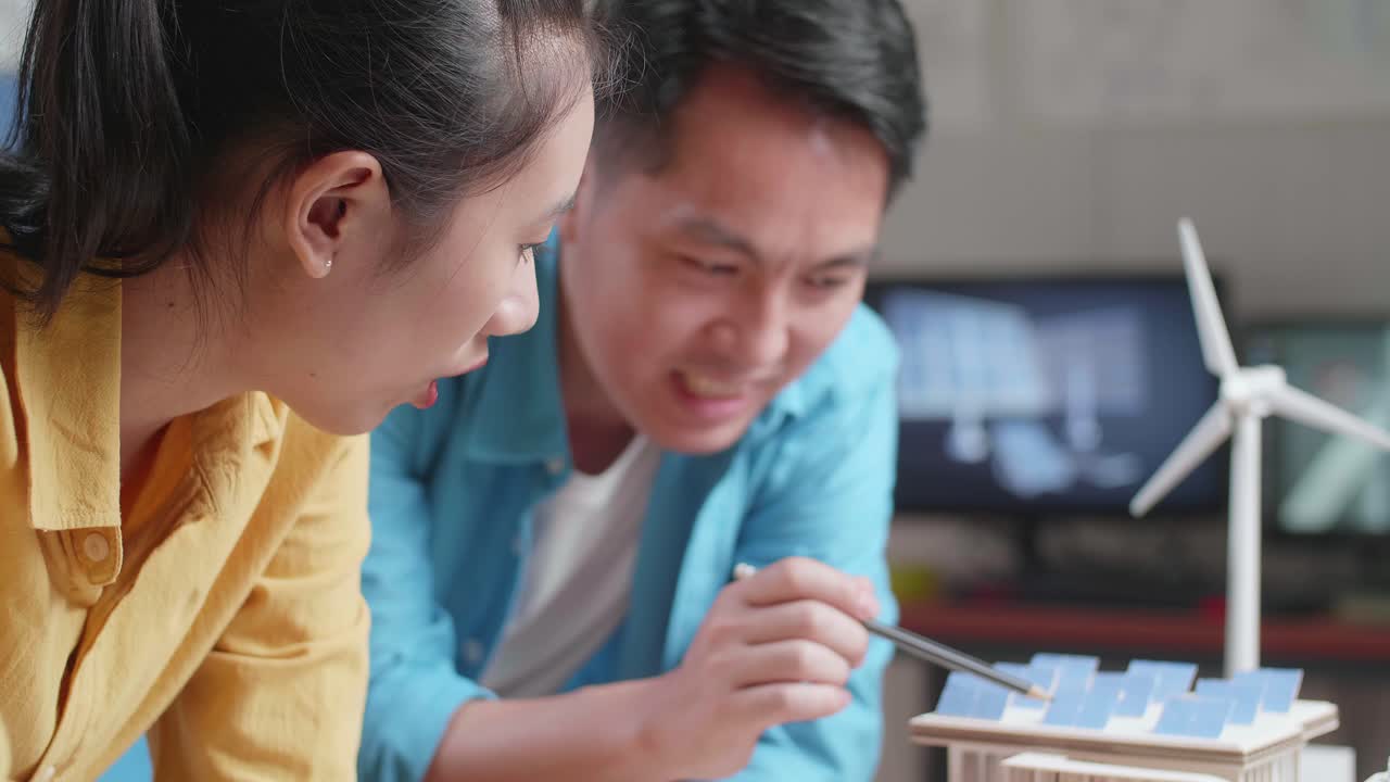 태양 전지 패널이 있는 작은 집의 모형을 만드는 데 서로 도움을 주는 아시아인 남녀의 클로즈업