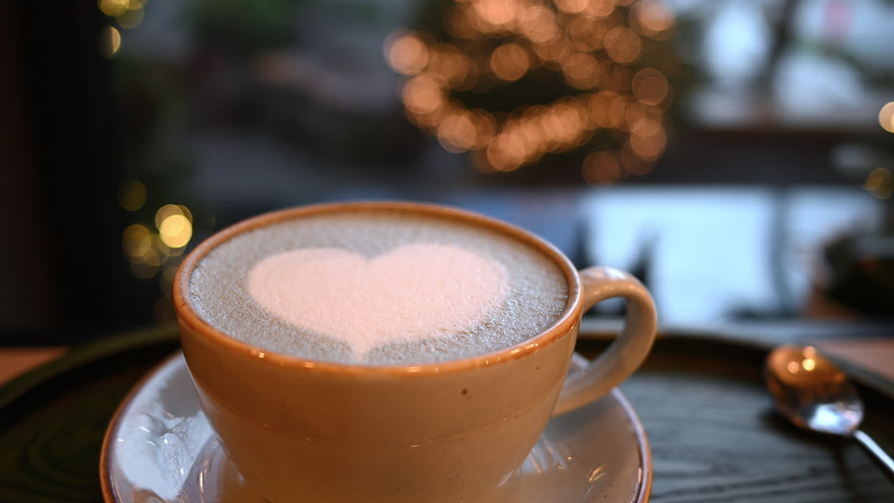 Cup of coffee with foam latte art in heart shape. Christmas tree on background