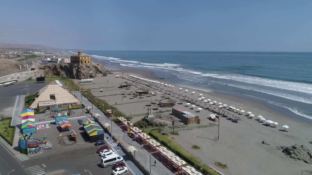 Stunning aerial view of a vibrant beach with lined umbrellas, blue ocean waves, and a lively amusement area. Ideal for travel blogs, tourism ads, and marketing visuals. Mollendo, Arequipa, Peru.