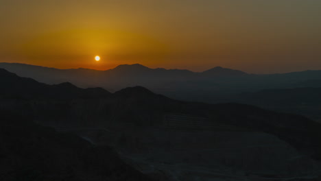 A-drone-timelapse-tilts-up-towards-the-sun,-setting-over-an-excavation-mine-pit-in-Pico-De-Los-Reales,-Estepona,-Spain