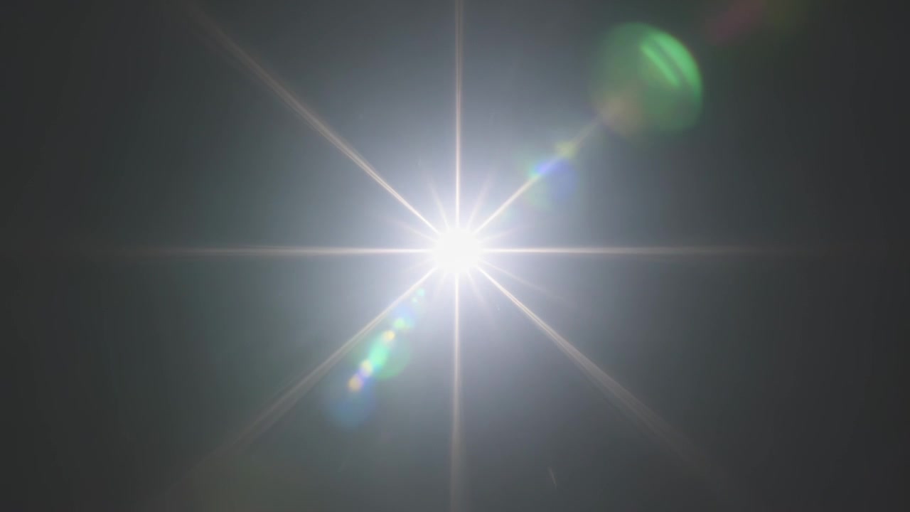 Luce centrale accecante che emette un bagliore crescente contro il cielo scuro, con bagliori dell'obiettivo, sfera verde, effetto a stella