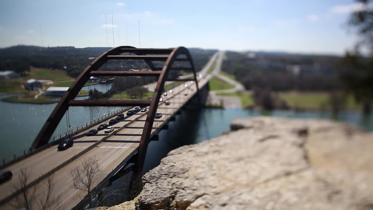 Austin Pennybacker Bridge, focus tilted to highlight narrow segment of ledge - front part of bridge. Traffic is heavy on north side, one lane has to stop while the other moves slowly.