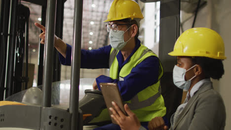 diverse male and female workers wearing face masks and using tablet in warehouse