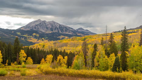 timelapse, clouds moving above yellow aspen forest and mountain peak