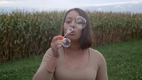 Mujer-Joven-Que-Sopla-Burbujas-En-El-Campo-De-La-Agricultura-Durante-El-Día-Nublado-En-La-Naturaleza