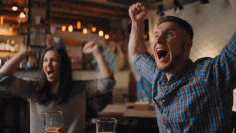 Close-up-of-a-group-of-fans-of-men-and-women-sitting-together-in-a-bar-and-watching-a-broadcast-on-TV-enjoying-a-goal-scored-shouting-and-hugging.-football-basketball-hockey.