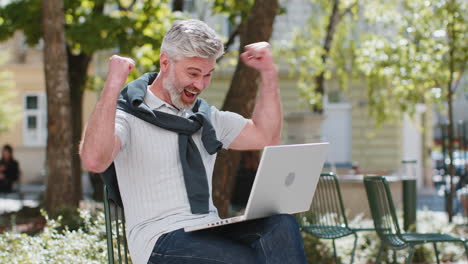 mature man using laptop computer celebrating win good message news lottery jackpot casino victory