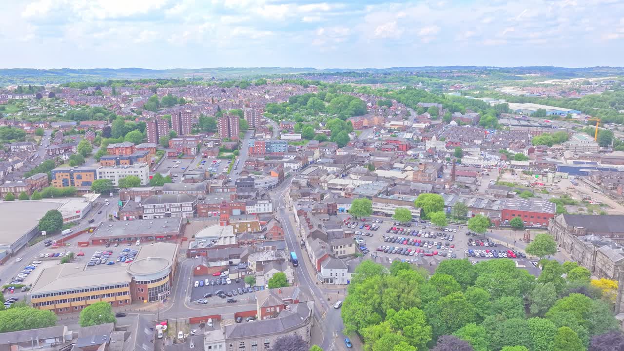 Forward-moving aerial view over Stoke city, UK, revealing mix of residential housing, tall apartment blocks, parking areas, and tree-lined streets under bright daylight sky