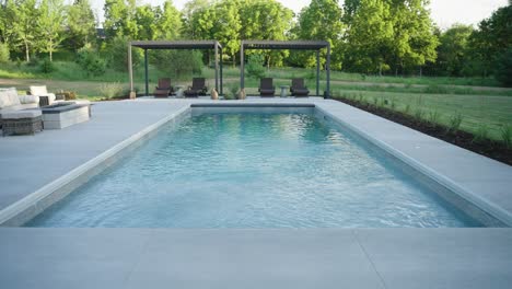 ground-level view of fiberglass pool, pergolas, and modern patio in lush setting