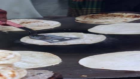 a chef cooking flatbread on a griddle in a street food stall