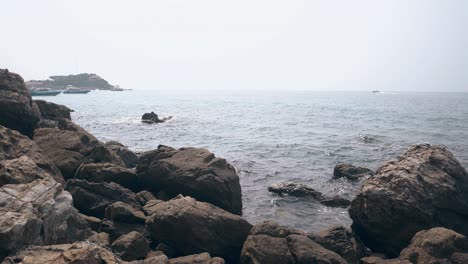 Grandes-Rocas-Grises-Desnudas-Contra-El-Océano-Azul-Ondulado-Con-Barcos