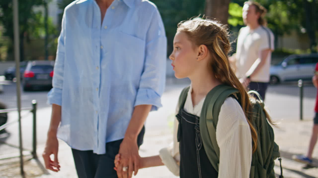 Closeup schoolgirl strolling mom at sunny street. Walking child talking parent