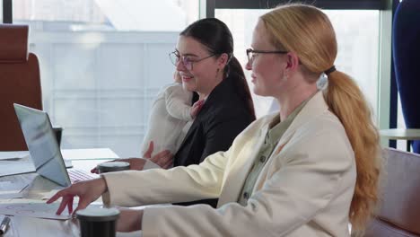 a businesswoman girl in round glasses and business clothes holds her little child in her arms while taking part in a meeting of colleagues at the table in the office
