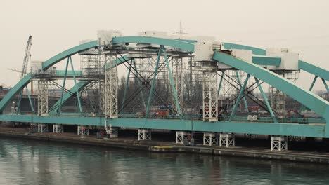static shot of a large bridge frame with aqua steel beams, scaffolding and construction equipment over a canal