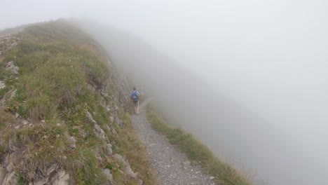 man hikes alone, walks into fog on narrow mountain trail in swiss alps