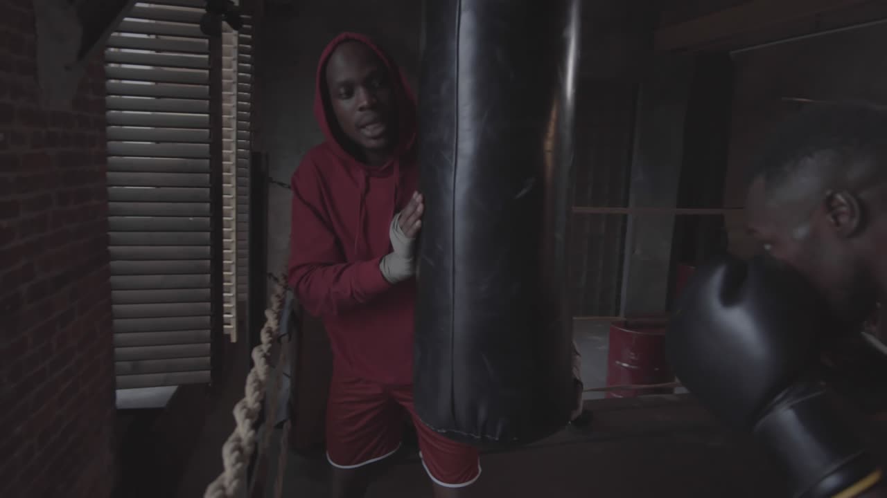Allenatore nero che regge il sacco da boxe per un pugile maschio in un fight club