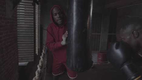 black coach holding punch bag for male boxer at fight club