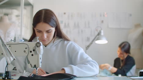 Tailoring-of-clothes.-Seamstresses-at-work-in-workshop-sewing-clothes-on-sewing-machine.-Dressmakers-sews-clothes-in-atelier.-Two-women-seamstress.-Dressmaking-in-sewing-business.