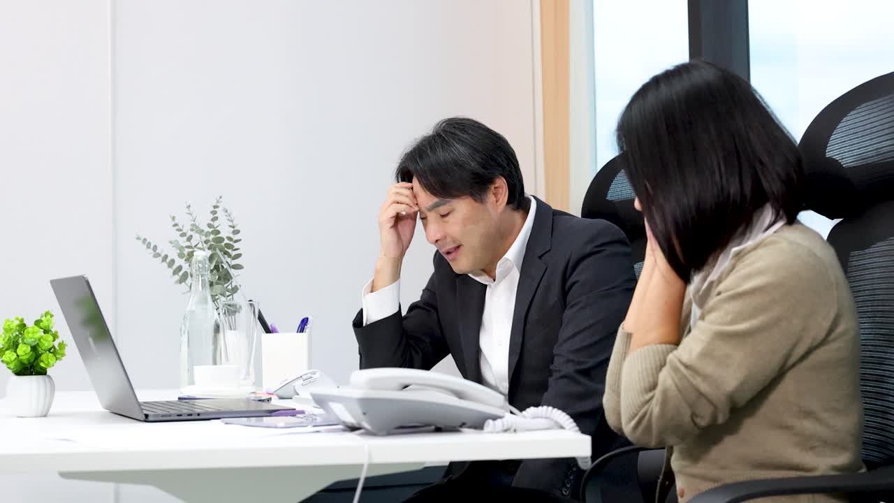 Two worried coworkers in modern office react anxiously to unexpected laptop video conference update
