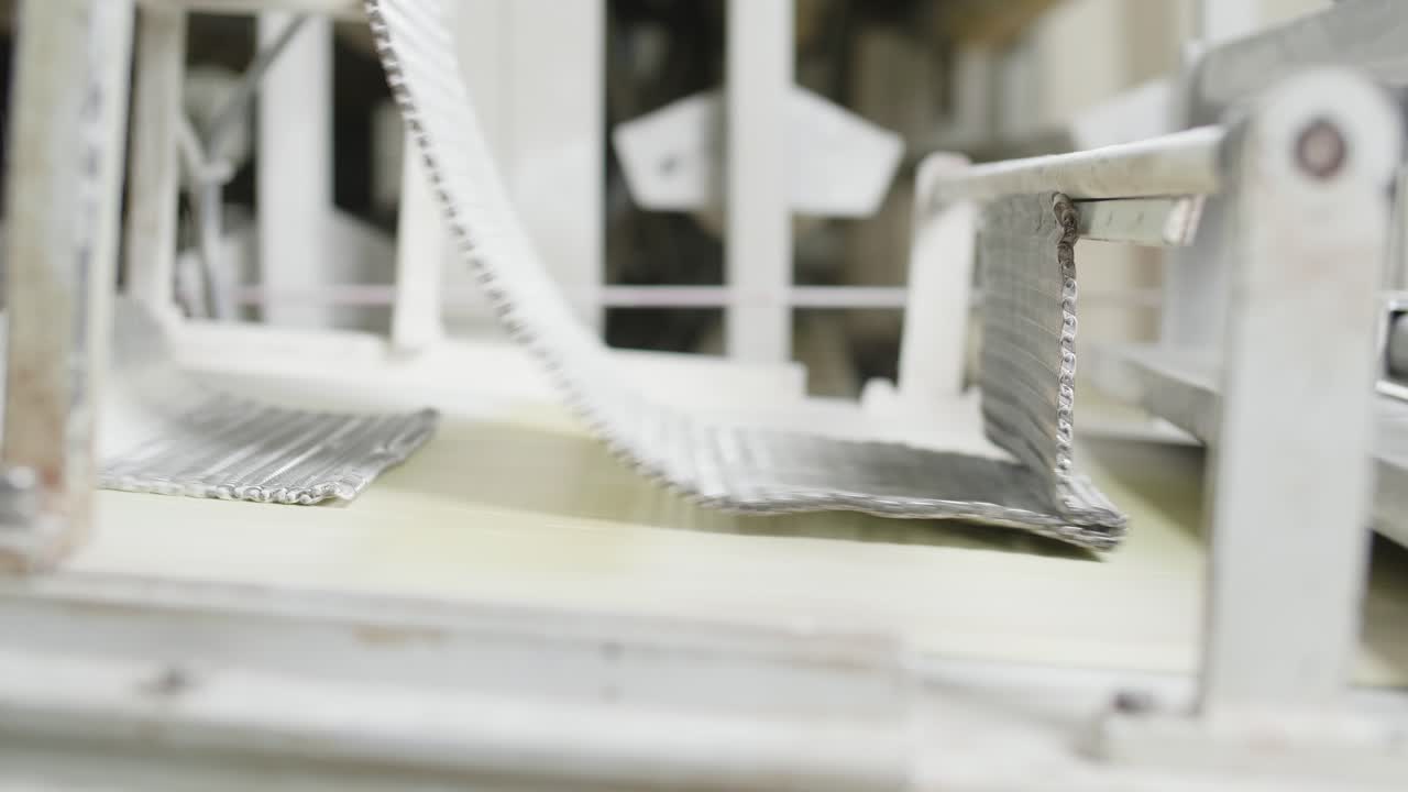 Fresh Bread Dough Being Rolled Underneath Chain mail On Conveyor Belt. Low Angle