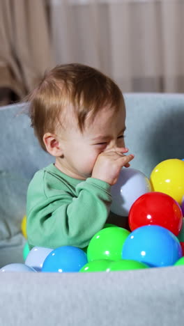 happy kid sitting in the soft basin with numerous balls. mommy throws the toys to her son. black domestic cat watching the baby. vertical video