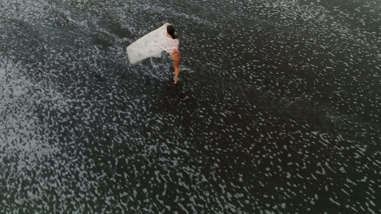 vista de pájaro abstracta tiro de drone de marea corriendo pasó girando, joven modelo en bikini