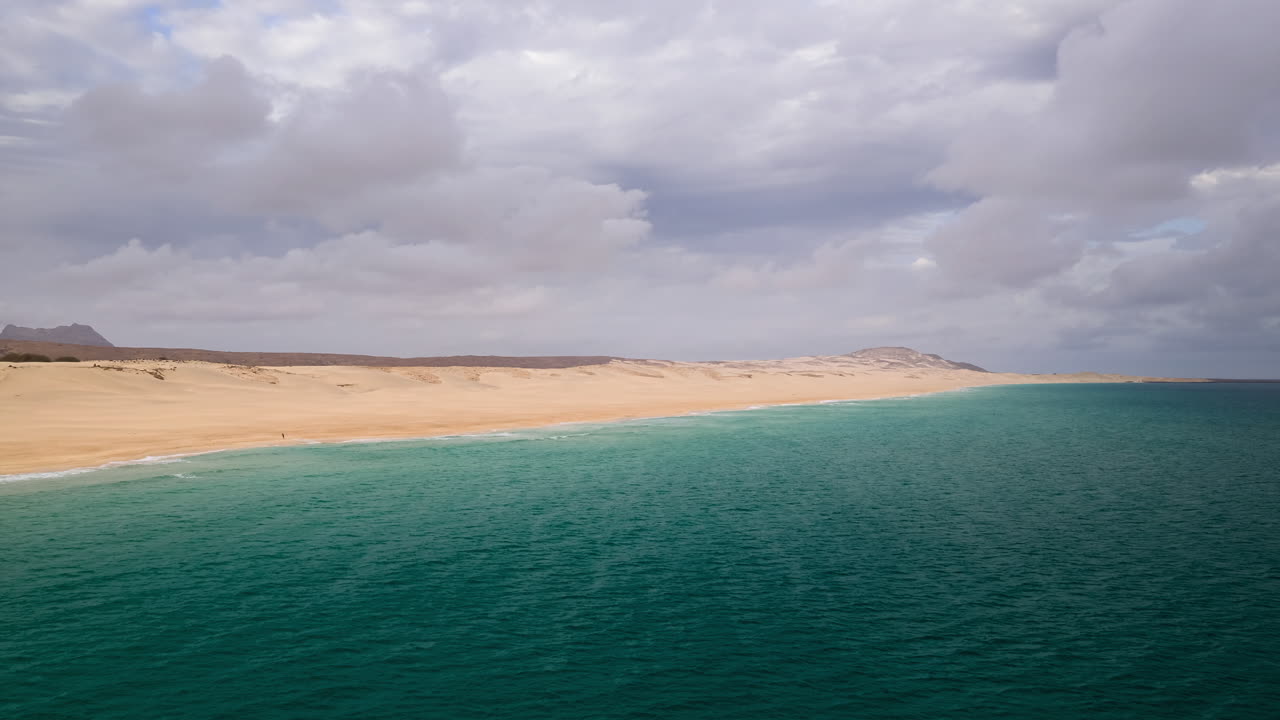 Drone view of a sandy beach, dunes and mighty waves of the Atlantic ocean at morning, background volcanic mountain, Boa Vista, Cape Verde