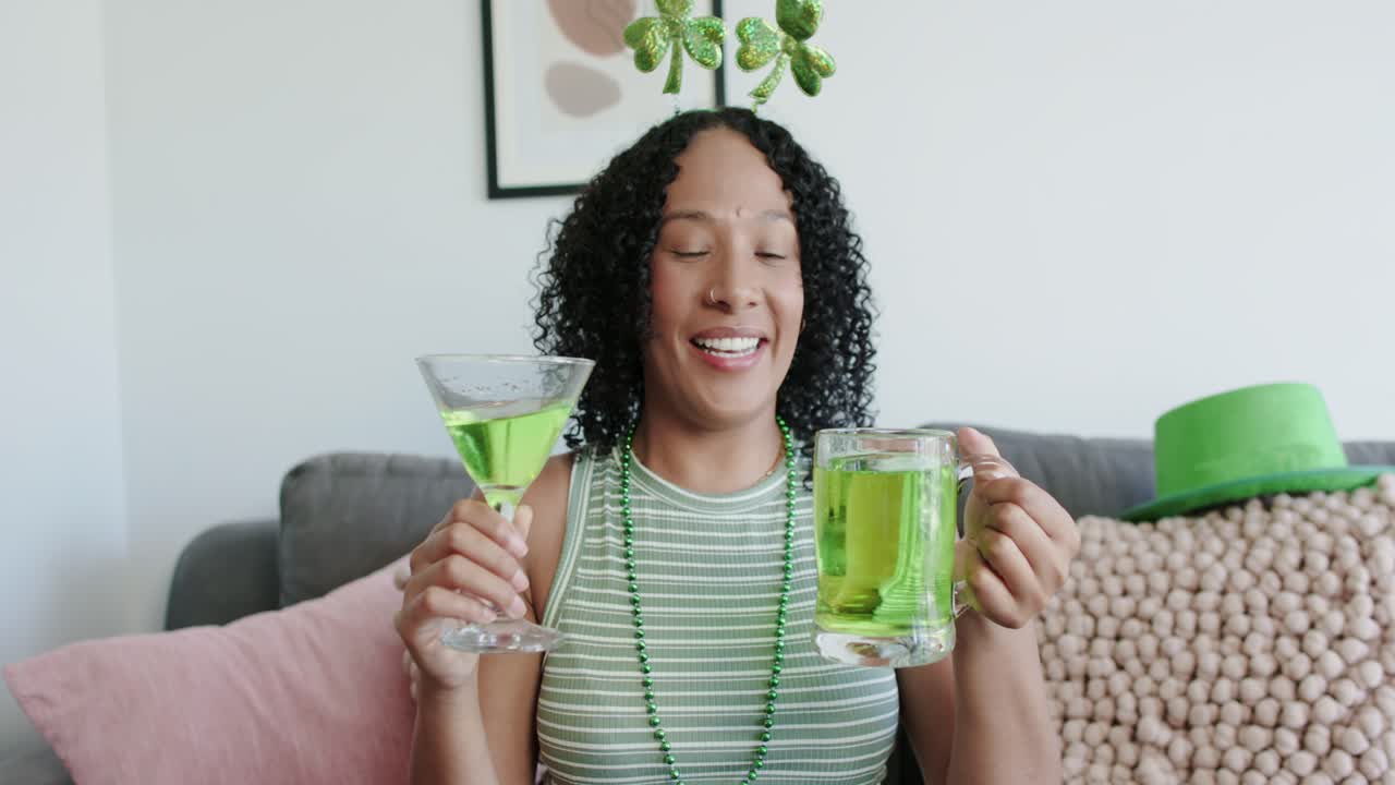 Yeşil boncuklu, Afrikalı Amerikalı bir kadın, kanepede oturmuş, yonca figürü eşliğinde martini ve bira bardağını kaldırıyor.