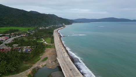 Flyover-drone-shot-of-coastal-highway-alongside-scenic-ocean-shoreline-at-island-of-Catanduanes,-Philippines