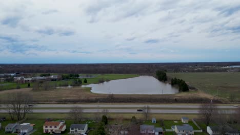 una imagen aérea que muestra un barrio residencial adyacente a una carretera, con un cuerpo de agua y campos abiertos en el fondo