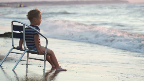 Niño-Sentado-En-La-Silla-Junto-A-Las-Olas-Del-Mar-Lavándose-Los-Pies