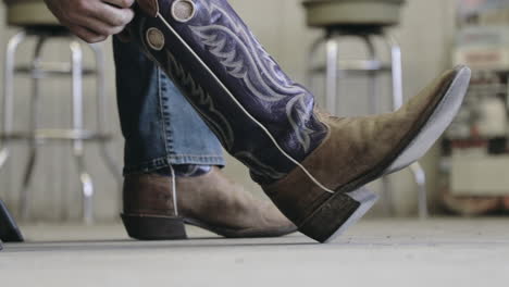 sitting man putting on cowboy boots and pulling jeans over