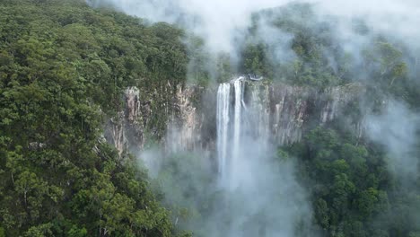 vista cinematográfica de la ladera de una montaña cubierta de niebla que revela una majestuosa cascada que se derrama sobre el acantilado de riolita.