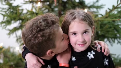 little brother kisses his sister on the cheek little brother kisses his sister on the cheek happy family on the background of the christmas tree children play and laugh