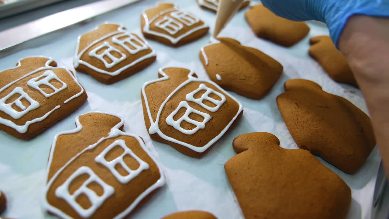 Handmade decoration of cookies at confectionery. Putting white glazing on a beautiful gingerbread houses. Close up.