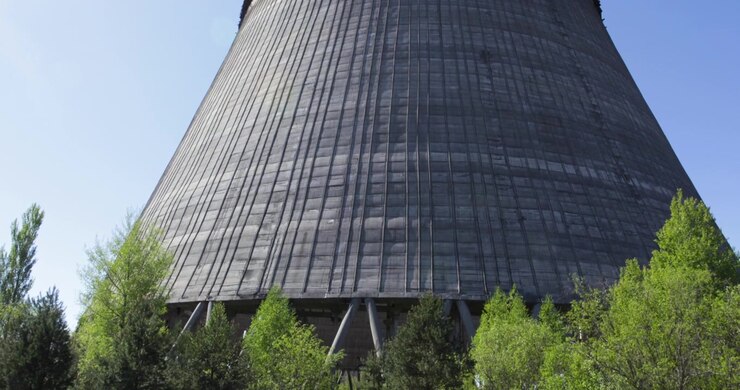 La telecamera inquadra dal basso verso l'alto una torre di raffreddamento in cemento incompiuta a Chernobyl