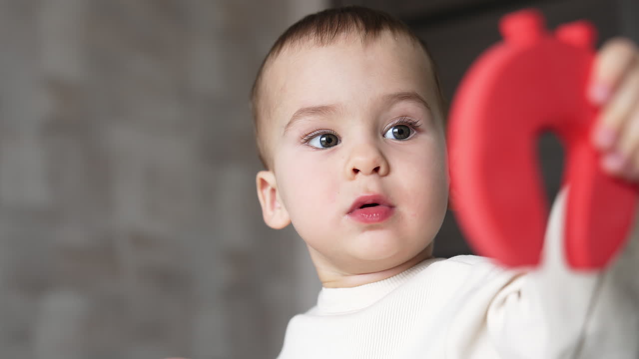 Beautiful Caucasian baby showing a toy to the camera. Lovely child looks attentively at the toy. Close up.