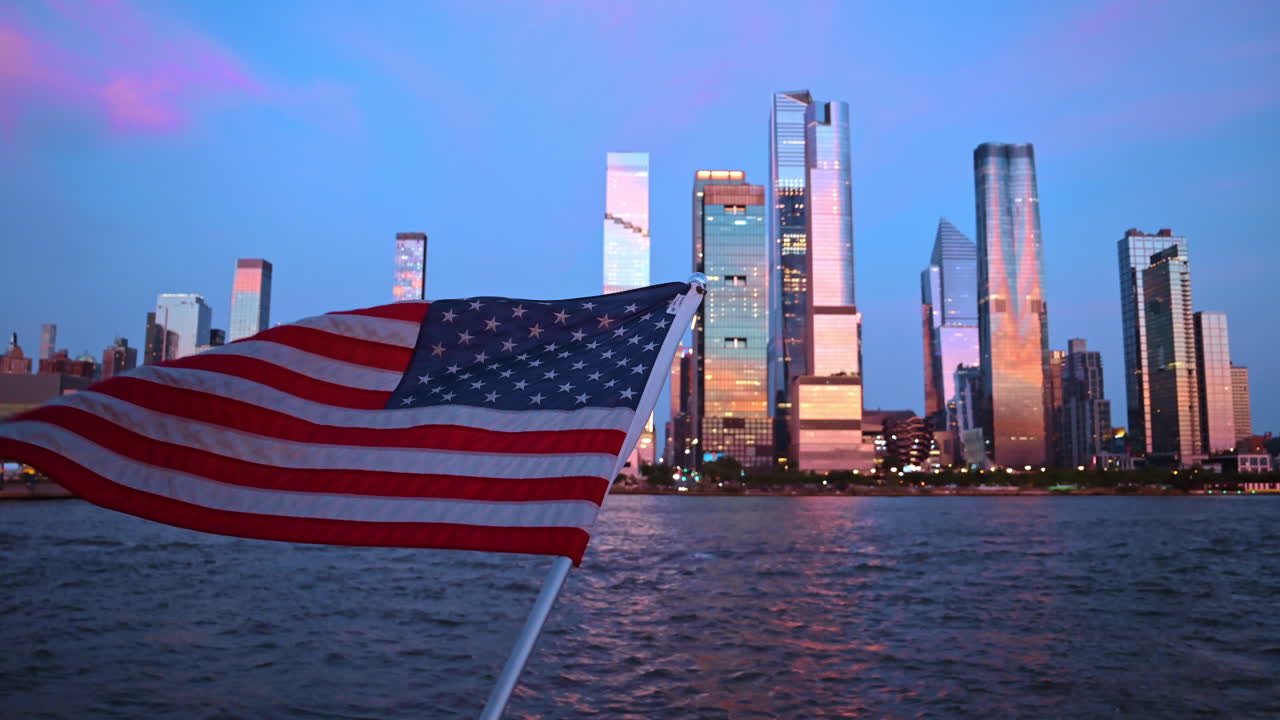 Bandiera statunitense che sventola con lo skyline di Hudson Yards come sfondo. Bandiera americana in primo piano con i moderni grattacieli di Hudson Yards durante l'ora blu.