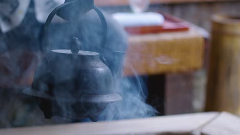 traditional japanese kettle hangs over smoky fire pit to boil hot water