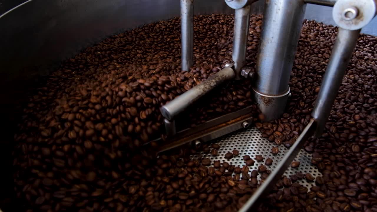 Freshly roasted dark brown Arabica coffee beans cooling and turning in industrial coffee roasting machine, close up of delicious coffee beans during roasting process