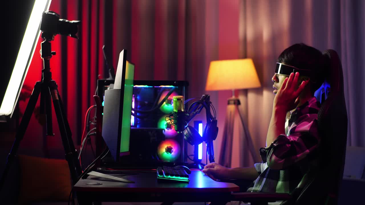 Side View Of Asian Boy Streamer Playing Game, Touching, And Swiping Experience Virtual Reality In Futuristic Goggles. Green Screen Personal Computer On Desk Illuminated By Rgb Led Strip Light