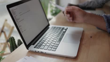 Man-holding-papers-and-using-laptop-in-coffee-shop