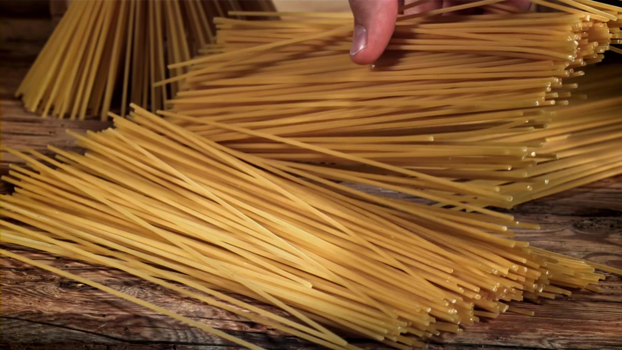 Mano che sistema spaghetti crudi su un tavolo di legno rustico