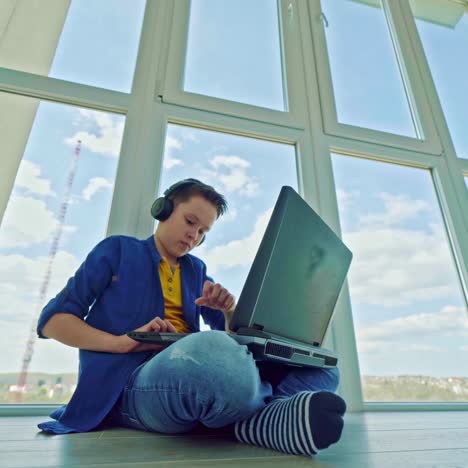 gaming at home. boy playing video games in his leisure time. teenager in earphones sitting near the window and playing on a laptop. happy boy wins the game.