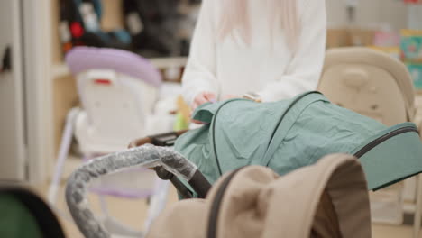 lone shopper opens closes stroller canopy in bright baby aisle, inspecting cover seams for damage, testing fabric resilience and canopy movement to evaluate pram quality in retail aisle