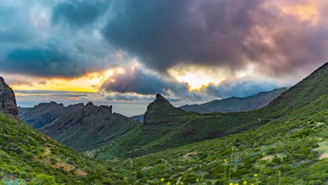 Die-Sonne-Geht-über-Einer-Grünen-Bergkette-Unter,-Mit-Ziehenden-Wolken-Und-Orangefarbenen-Sonnenstrahlen,-Die-Durch-Die-Berge-Brechen