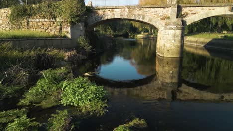 Volando-Bajo-El-Antiguo-Puente-De-Piedra-Que-Cruza-El-Río-Anllons-En-Ponteceso,-A-Coruña,-España