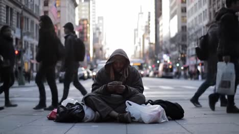 a busy city street showcases a multitude of pedestrians moving about their day. amid the rush, an individual sits on the ground, surrounded by bags, highlighting the contrast of urban life.